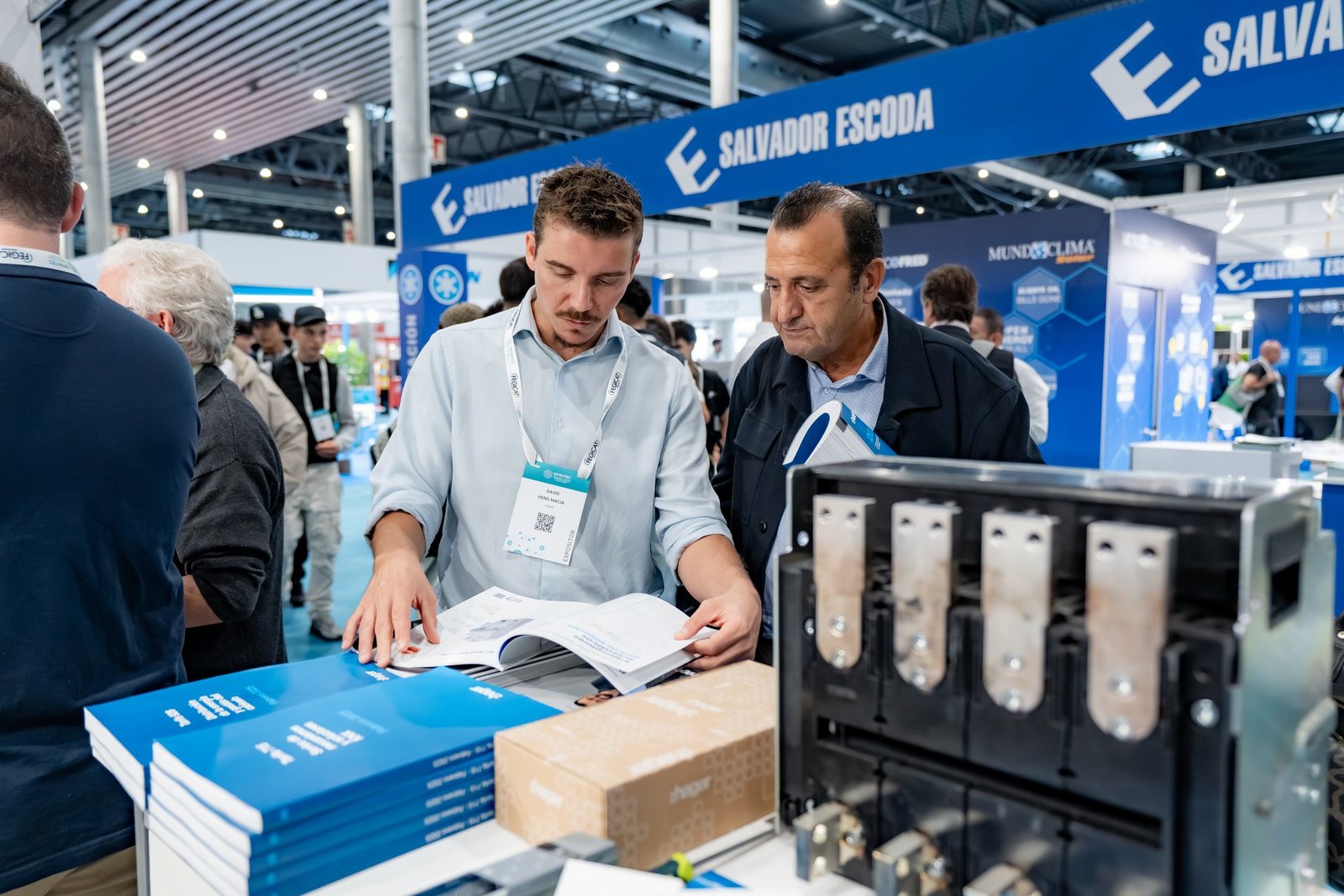 Dos hombres revisan folletos de Hager en un stand de la feria Efintec. Uno lleva acreditación de expositor.